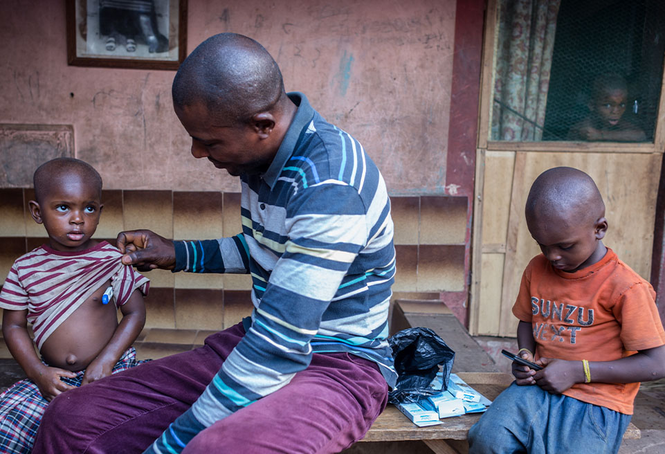  M. Agu vérifie la température de sa fille lors d'une visite hebdomadaire d'ALIMA dans les communautés afin de rechercher des cas et prévenir la progression de l'épidémie